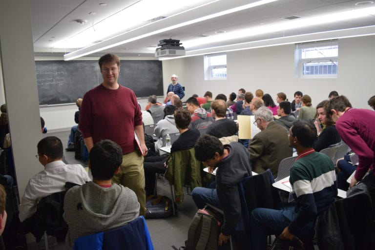 a guy wearing a red sweater standing in front of one of the participants during lecture